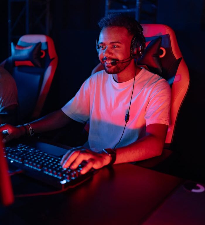 An African American man engaged in gaming at a computer station, wearing a headset.